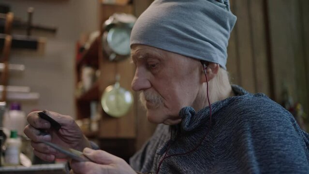 Senior gray haired male master in a wheelchair working at his workshop sharpening japanese deba knife