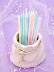 A vase in the form of a bag with pastel candles on a pale lilac background with pearls