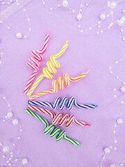 A set of multicolored candles in the form of a spring on a pale lilac background with pearls