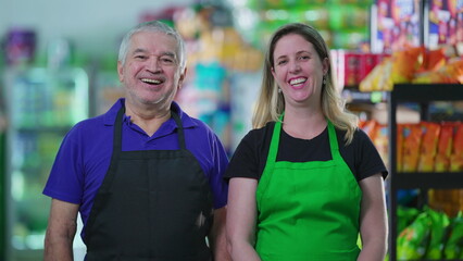 Portrait of two happy employees of supermarket business with smiling expressions. A senior caucasian male staff manager next to a middle-aged female worker