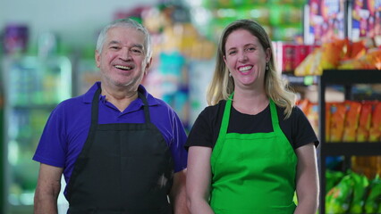 Portrait of two happy employees of supermarket business with smiling expressions. A senior caucasian male staff manager next to a middle-aged female worker