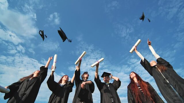 Joyful graduates stand in a row and toss their caps up in the air.