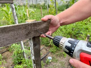 Obraz premium A tough construction worker applies wooden siding to a garage and drills screws