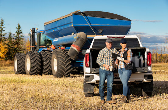 Farm couple uses tablet to monitor fall canola harvest while taking a coffee break, Alberta, Canada