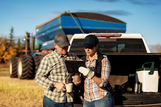 Farm couple uses tablet to monitor fall canola harvest while taking a coffee break, Alberta, Canada