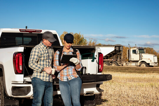 Farm couple uses tablet to monitor fall canola harvest while taking a coffee break, Alberta, Canada