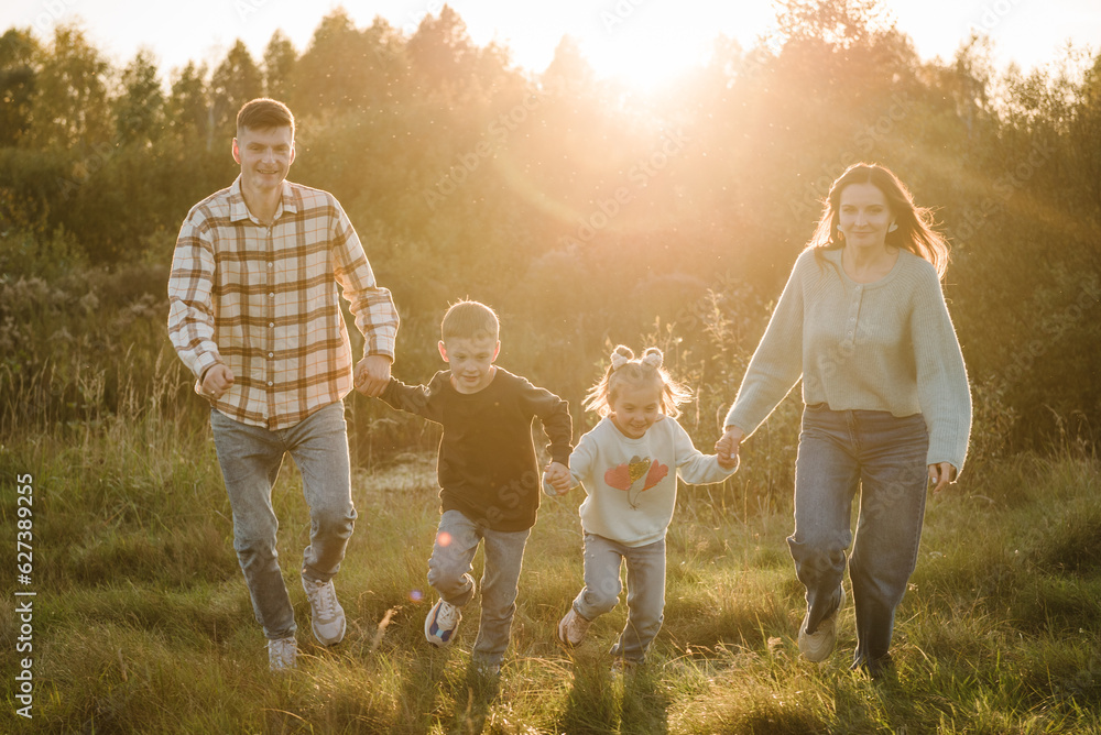 Wall mural happy young family with children spending time together, running outside, go in nature at sunset. mo