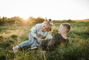 Naklejka na ściany i meble Happy children walking spending time together in nature. Kids playing in mountains on autumn day. Daughter, son hugging, lying in green grass in field at sunset. Portrait child in summer. Closeup