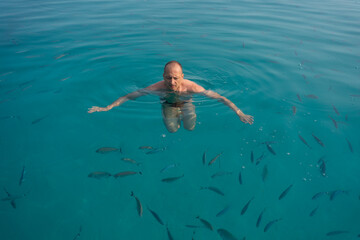 a man swims in a turquoise sea full of fish