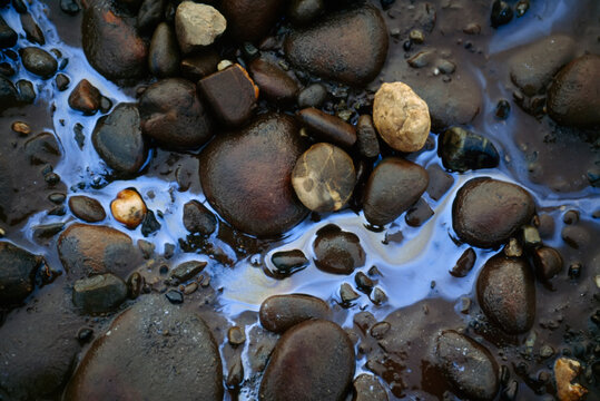 Oil slick and pebbles in a stream; North Slope, Alaska, United States of America