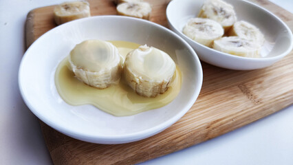 Sliced round Pieces of Banana on white plate and on wooden board on white background. Banana cooking, Close up. Delicious sweet fruit dessert