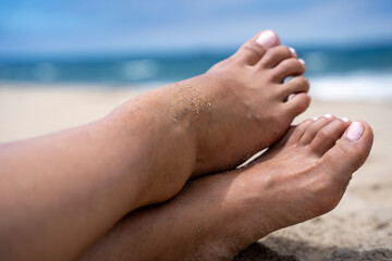 Close up of a woman's bare feet, crossed at the ankle, relaxing on the beach.