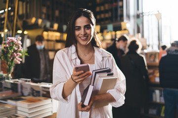 Smiling woman standing with smartphone in bookstore