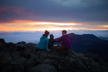 Fototapeta premium Family on a mountain top above the clouds at Haleakala watching the sunrise over the Pacific Coast; Haleakala National Park, Maui, Hawaii, United States of America