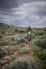 Obraz premium Female Dirt biker through sage brush desert terrain with stormy sky back drop near Twin Falls Idaho