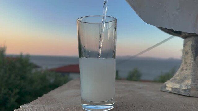Close up shot of Turkish, Greek alcoholic drink raki near seaside, evening time. Pouring raki and water.