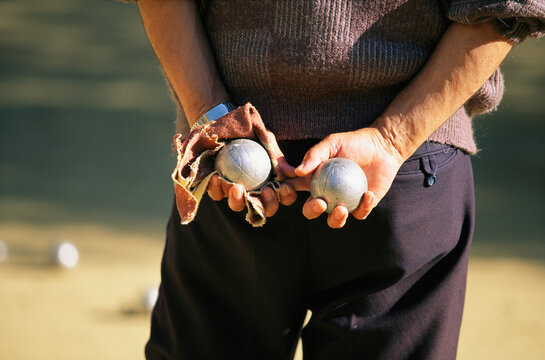 Man stands holding two bocce balls behind his back, waiting his turn to play; Barcelona, Spain