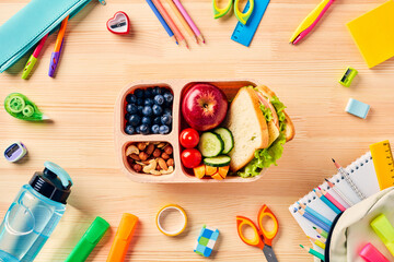 School lunch box with healthy food and school supplies on wooden table. Back to school concept. Top...