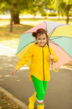 Little cute girl kid child in a yellow raincoat with multicolored rainbow umbrella