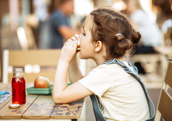 Cute little schoolgirl eating from lunch box outdoor sitting on a school cafe. Food for kids.