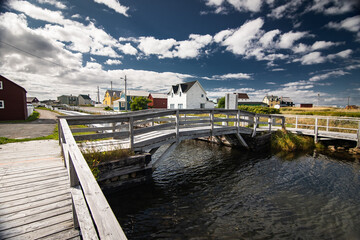 Wooden boardwalk and bridge over a canal with distant East coast beach homes on Bonavista Newfoundland Canada.