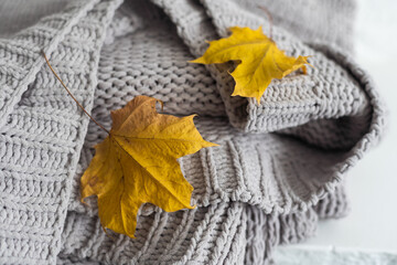 Fototapeta na wymiar Yellow and Ultimate Gray. Crop of stack gray woolen knitted blankets, warm plaids decorated maple leaf, autumn cozy concept