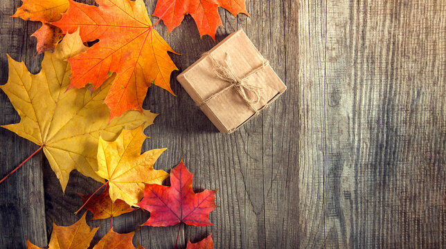 cardboard box tied with string on a bow on a wooden background in autumn leaves, holiday gift on Thanksgiving Hellouin. view from the top. copy space