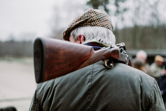 Older man on a hunt. Senior hunter with grey hair, tweed cap and oilskin jacket carrying a shot gun on his shoulder. Pheasant hunting in fall