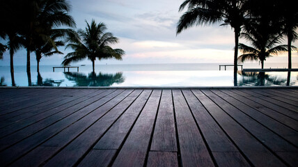 Close up of wooden floor of swimming pool with view of sunrise and some coconut trees. holiday at...