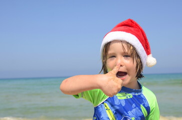 Cute boy in santa hat on the beach. The concept of vacation at sea, family holidays in December....