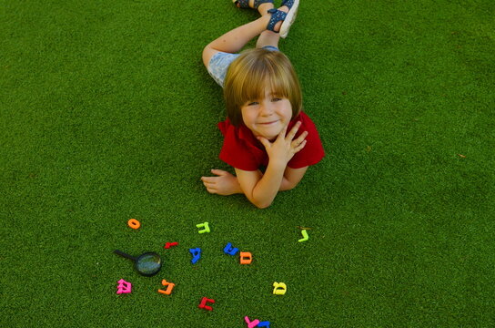 Hebrew alphabet. The boy is learning Hebrew. Multi-colored letters on the grass. The child is preparing for the Israeli school. Repatriation, aliya.