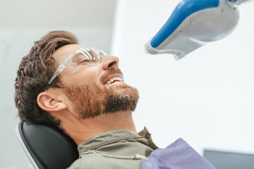 Handsome joyful male patient using ultraviolet lamp after making filling