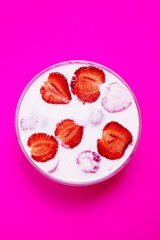 Top view of glass bowl with strawberry yogurt on pink background. Strawberry yogurt covered by fresh strawberry slices. 