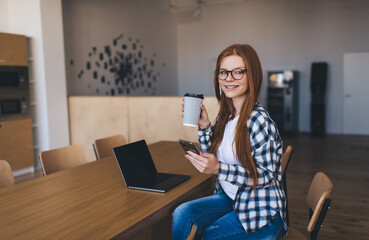 Smiling woman sitting at cafe with smartphone and laptop