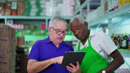Senior Manager Presenting Tablet Screen to Senior African American Grocery Store Employee