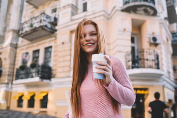 Cheerful woman standing on street with coffee to go
