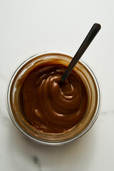 Salted Caramel sauce in glass bowl on white marble background. Butter, sugar with cream and salt. 