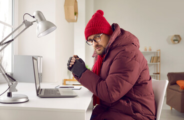 Man in warm clothes freezing indoors in a very cold winter. Man wearing a warm winter coat, hat and...