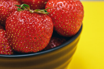 Ripe strawberry. Black bowl with strawberries on yellow background. Strawberry closeup.