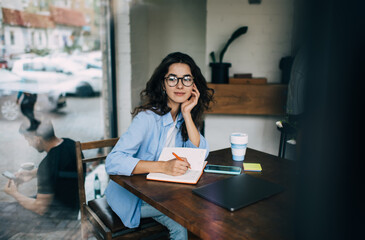 Pensive woman writing thoughts in diary at cafe table