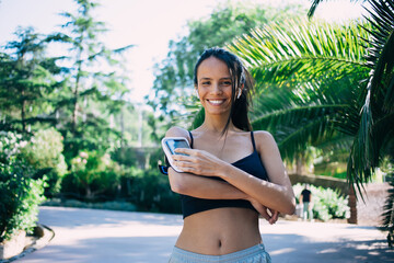 Smiling ethnic woman standing and using smartphone in armband