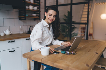Smiling female freelancer checking messages on smartphone while using laptop