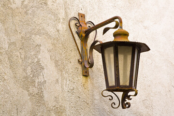 Italian rusty streetlight of nineteenth century against a plaster wall