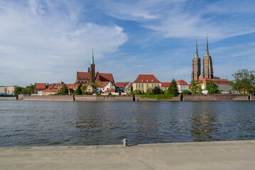 Outdoor view on the waterside of Oder river and background of Archbishop's Palace, Collegiate Church of the Holy Cross and St. Bartholomew and Wieża Katedry św. Jana Chrzciciela in Wroclaw, Poland. - obrazy, fototapety, plakaty