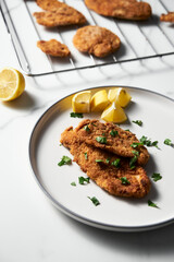 Baked Chicken Schnitzel on white plate with lemon. Rack or grid with baked schnitzel in breadcrumbs on background. 