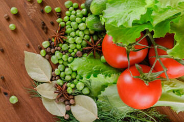 A set of several cucumbers, pea, dill, lettuce, tomato branch, bay leaf, pepper, anise, lie on the wooden table. Fresh raw organic vegetables closeup. Top view.