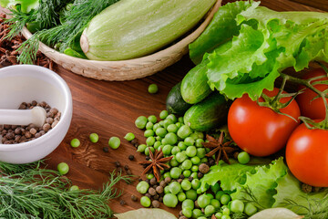 Fresh raw organic vegetables. A set of several cucumbers, dill, lettuce, tomato, zucchini, pepper, anise, bay leaf, spices, green peas lie on the wooden table. Closeup.