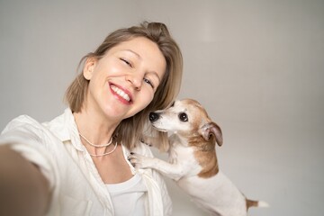 Selfie portrait of beautiful blonde smiling happy woman and her small cute dog Jack Russell terrier looking at camera and smiling. having fun wit the pet. Best friends ever! white shirt and blue jeans