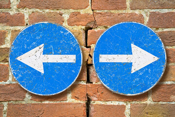 Old blue metallic arrow sign against an aged cracked brick wall indicating to go left and right -...