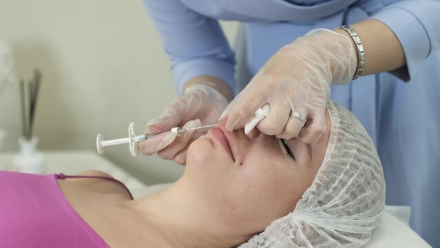 clip illustrates the biorevitalization process in a beauty clinic: a specialist injects hyaluronic acid into the patient's nasolabial folds to improve facial contour and reduce signs of aging